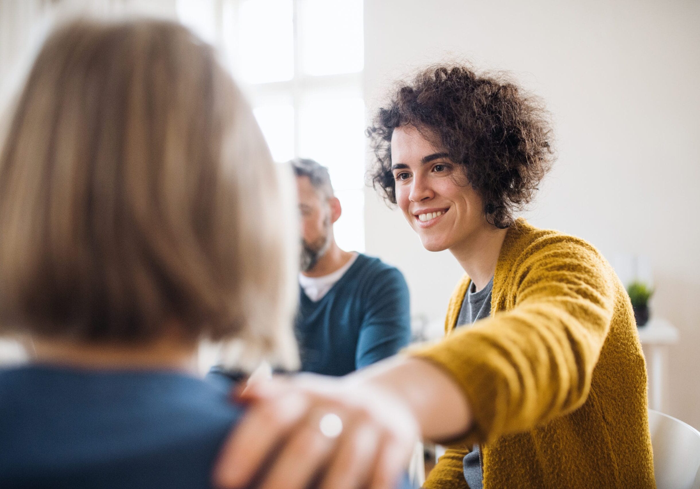 Serious men and women sitting in a circle during group therapy, supporting each other.
